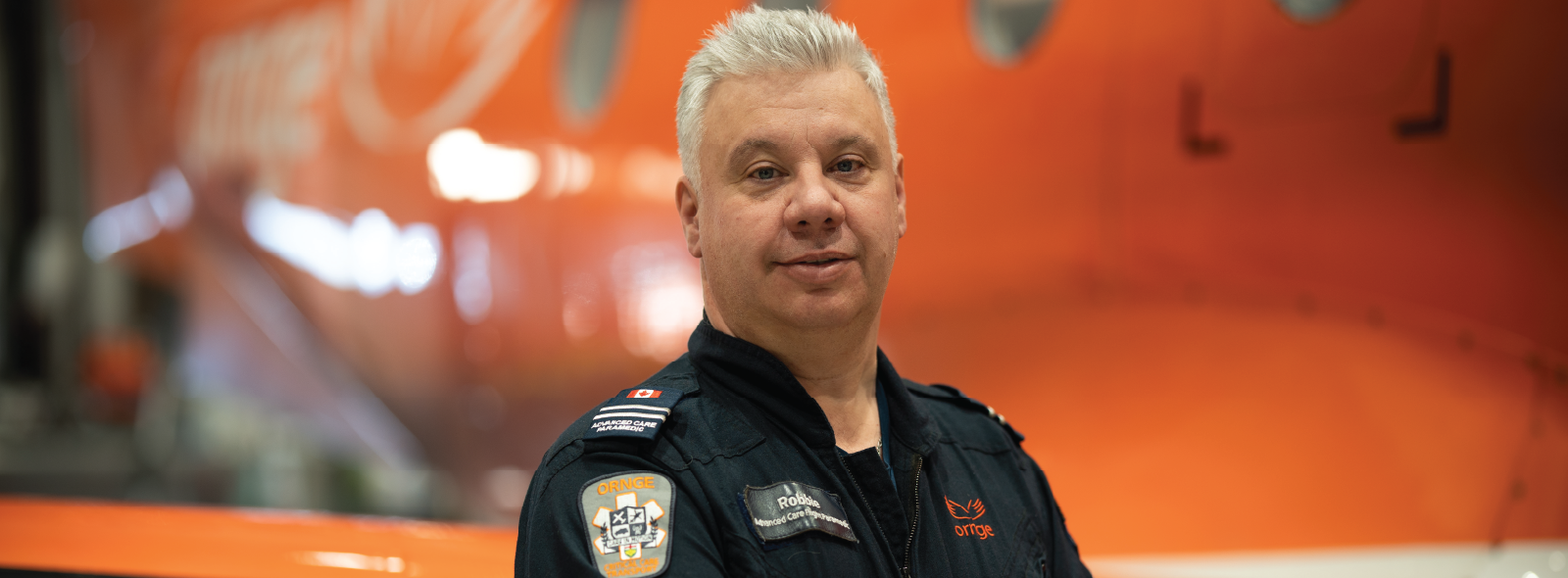 A paramedic in uniform standing in front of an orange plane
