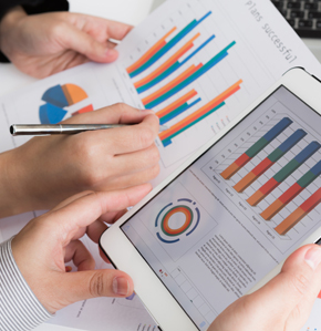 Hands holding a piece of paper and ipad with graphs and charts