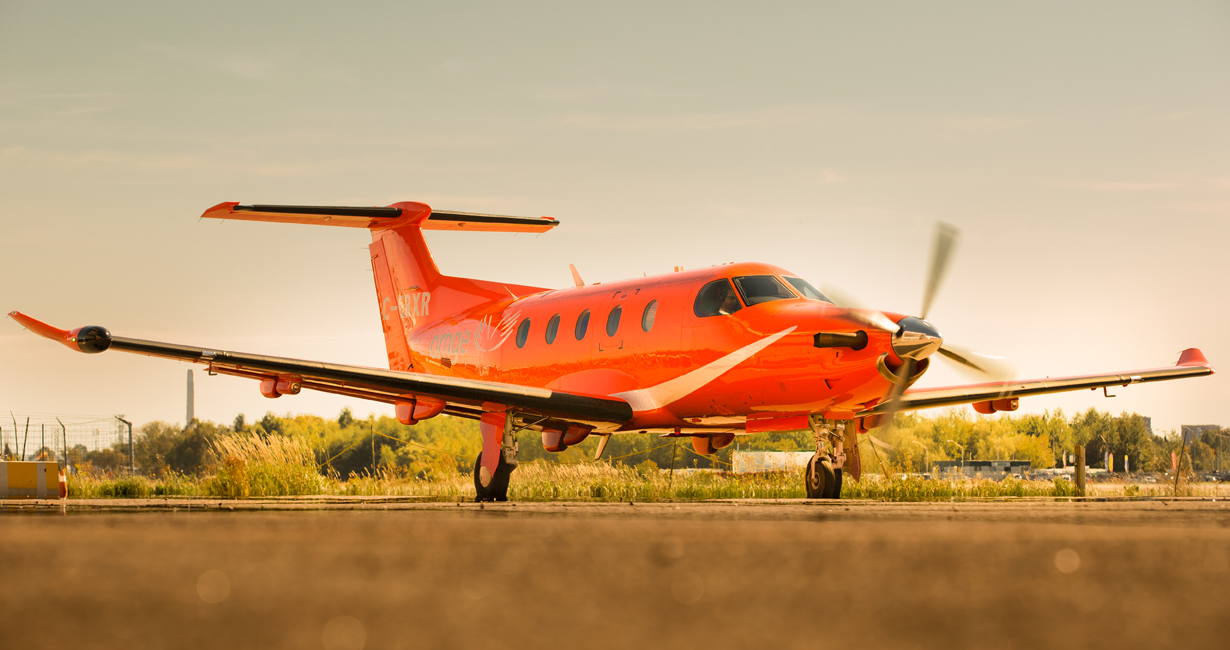 An Ornge Pilatus PC-12 airplane in front of an beautiful orange sunset sky