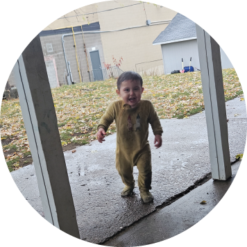 Person standing outdoors with a scenic view of a lush green landscape, palm trees, and a calm body of water with mountains in the background.