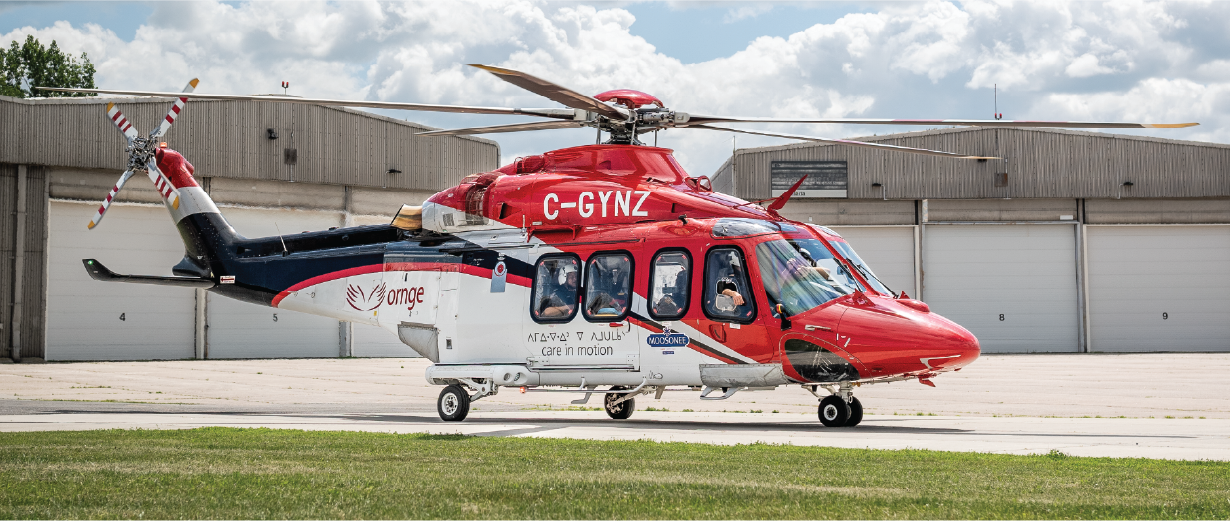 Un hélicoptère ambulance Ornge rouge et blanc est stationné sur une surface pavée devant un grand hangar.