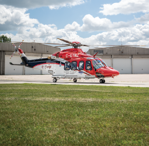Un hélicoptère ambulance Ornge rouge et blanc est stationné sur une surface pavée devant un grand hangar.