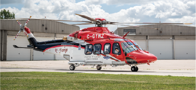 A red and white Ornge air ambulance helicopter is parked on a paved surface in front of a large hangar.