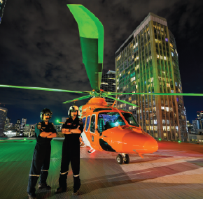 two pilots on a helipad next to an orange helicopter