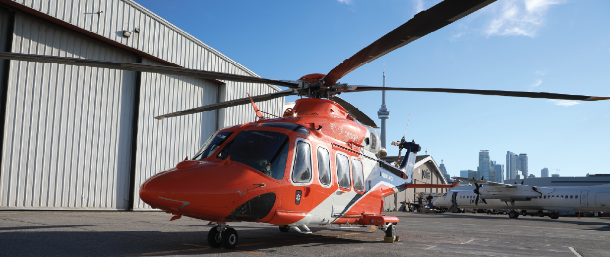 un hélicoptère orange sur le tarmac avec la tour CN derrière lui