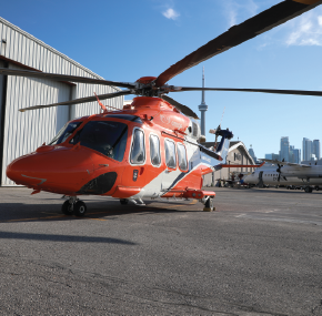 an orange helicopter on the tarmac with the CN tower behind it