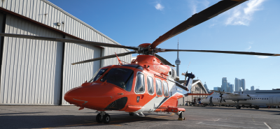 un hélicoptère orange sur le tarmac avec la tour CN derrière lui