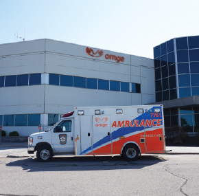 Une ambulance Ornge stationnée devant un immeuble de bureaux avec de grandes fenêtres et le logo Ornge affiché bien en évidence sur la façade.