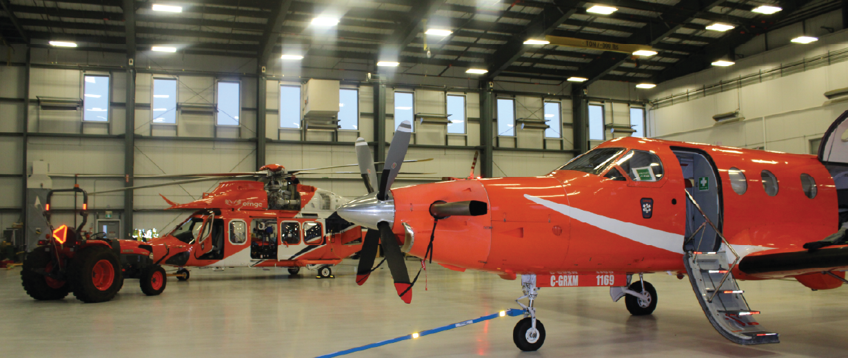 Two orange air ambulance aircraft and a helicopter inside a brightly lit hangar.
