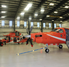 Two orange air ambulance aircraft and a helicopter inside a brightly lit hangar.