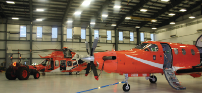 Deux avions ambulances aériennes orange et un hélicoptère se trouvent à l'intérieur d'un hangar fortement éclairé.