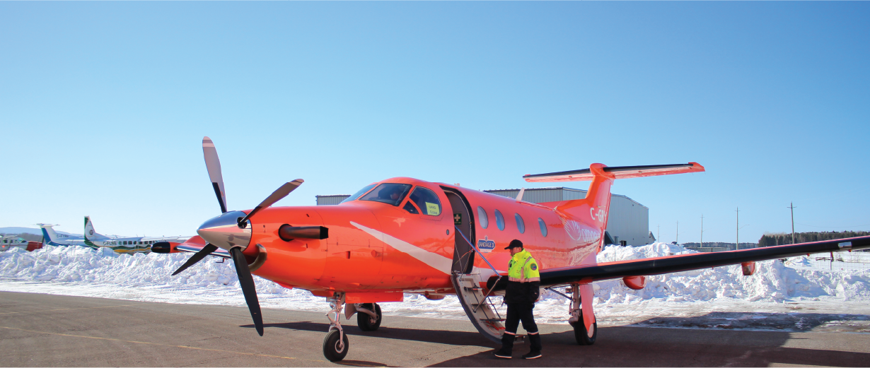Un avion ambulance orange stationné sur un tarmac enneigé, un membre d'équipage se tenant près de la porte ouverte.