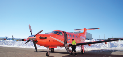 Un avion ambulance orange stationné sur un tarmac enneigé, un membre d'équipage se tenant près de la porte ouverte.