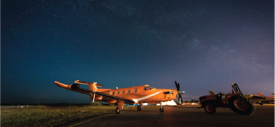 An orange air ambulance aircraft on a tarmac at night under a star-filled sky.