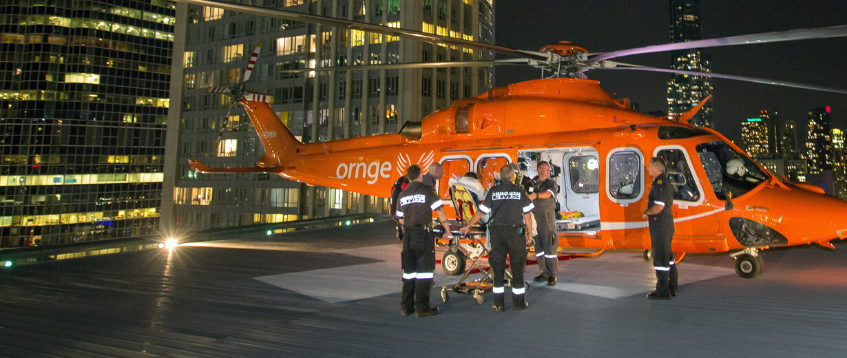 A group of Ornge paramedics bringing a patient on a gurney into an Ornge helicopter at night