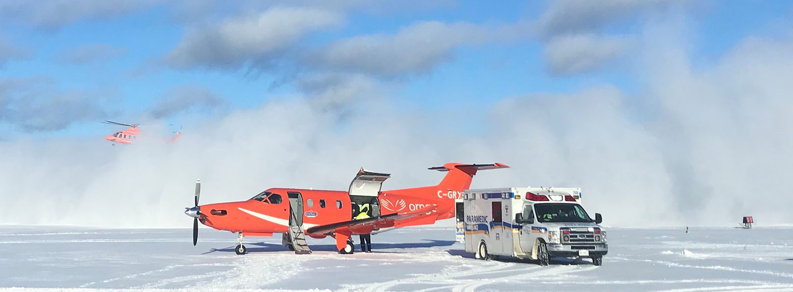 An Ornge fixed wing aircraft accepting a patient from Simcoe Paramedic Service and a helicopter landing in the background. 