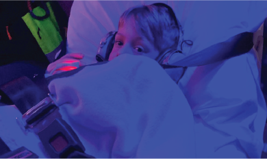 Patient secured on a stretcher with safety straps under blue and purple lighting inside a medical transport setting.