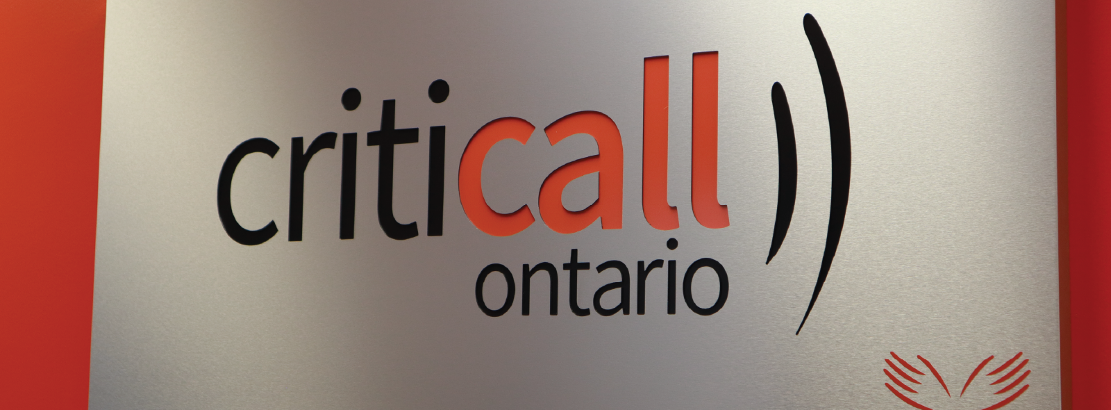 A rectangular sign mounted on a orange wall displaying the logo for CritiCall Ontario. The text reads “criticall ontario”