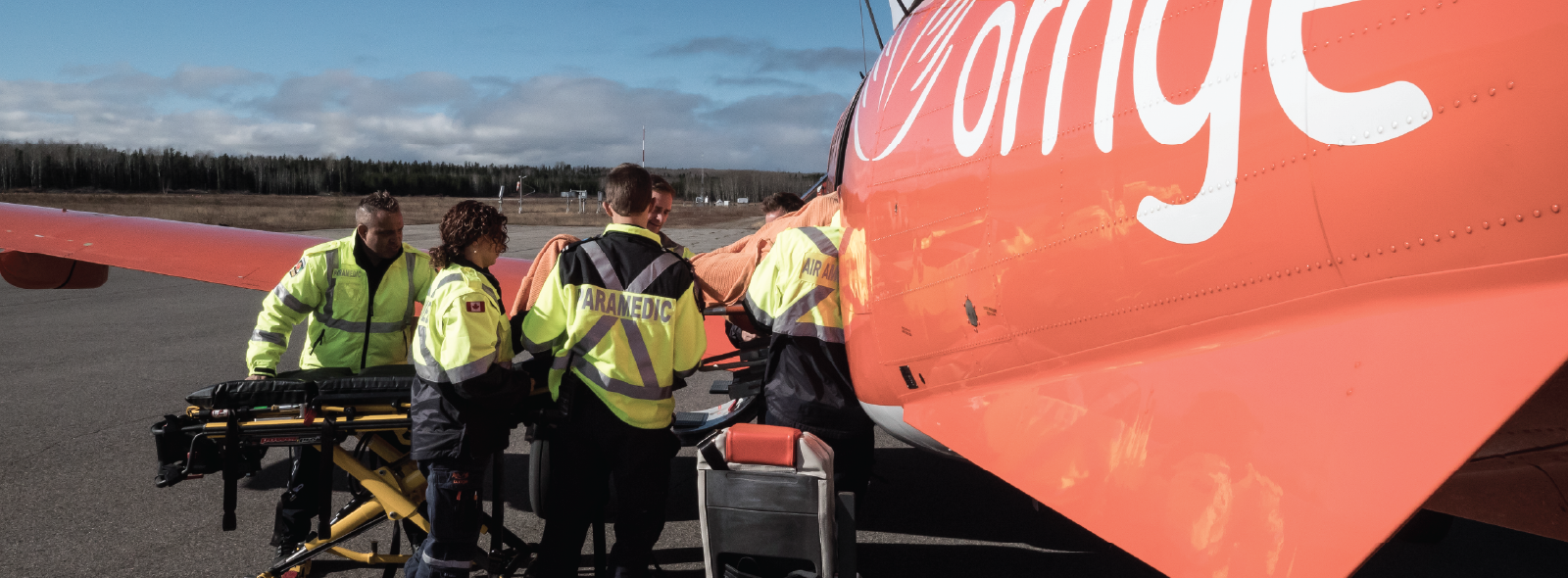 Paramedics transfer a patient to an orange Ornge air ambulance