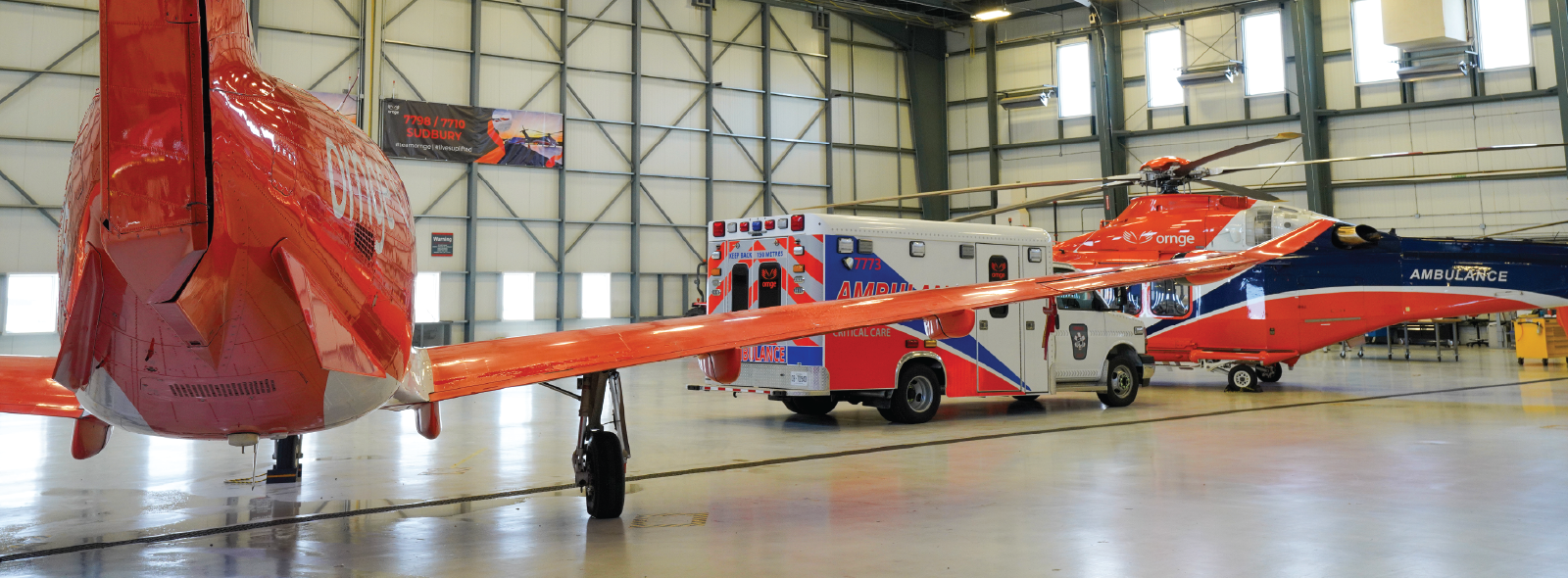 un avion orange à côté d'une ambulance et d'un hélicoptère orange à l'intérieur d'un hangar