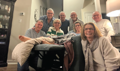 Un groupe de personnes âgées souriantes, réunies dans un salon, entoure une personne se reposant sur un canapé.