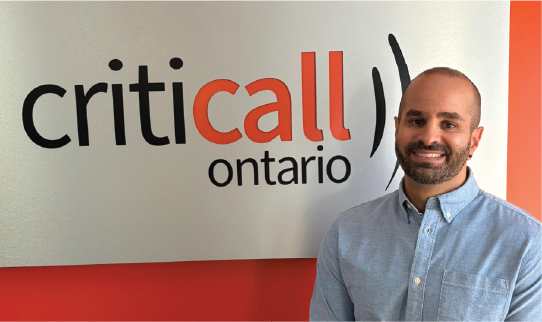 Person standing beside a wall sign that reads “CritiCall Call Ontario.”