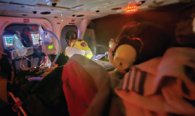 Medical crew caring for a patient inside an air ambulance with monitors and equipment illuminated.