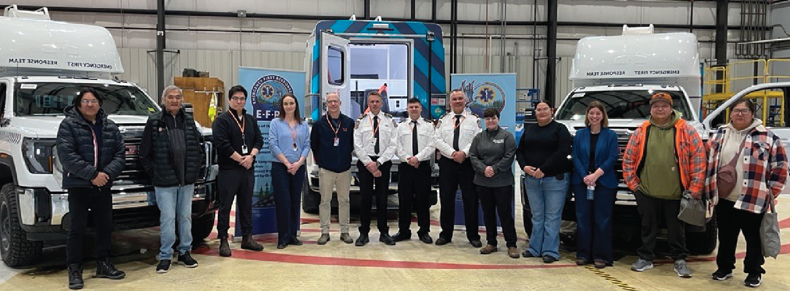 Group of people standing in a hangar between two medical transport vehicles with a blue emergency response truck in the background.
