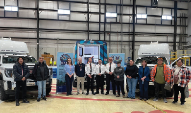 Group of people standing in a hangar between two medical transport vehicles with a blue emergency response truck in the background.
