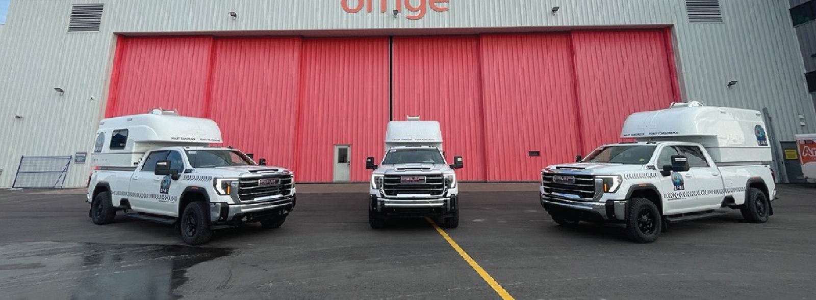 Three EFRT vehicles parked in front of a hangar with large red doors and the Ornge logo