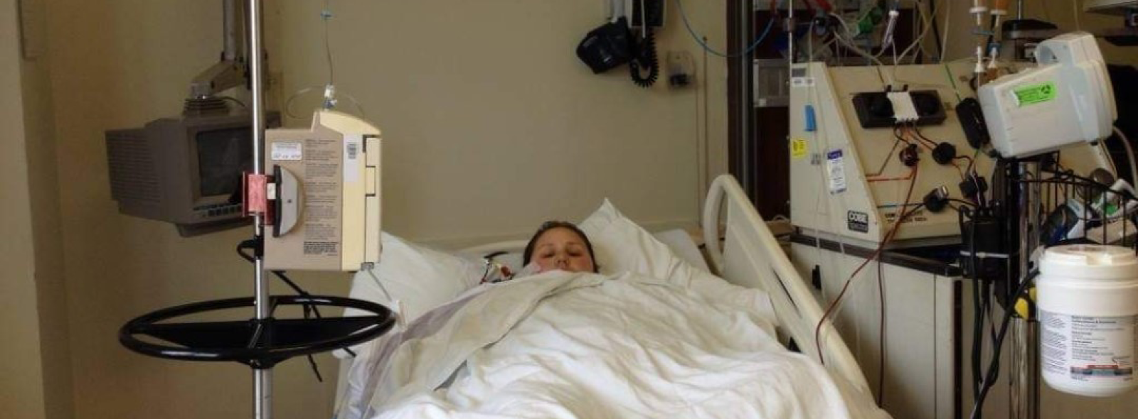 Annie Maynard laying down in a hospital bed with the blankets pulled up tightly around her face.