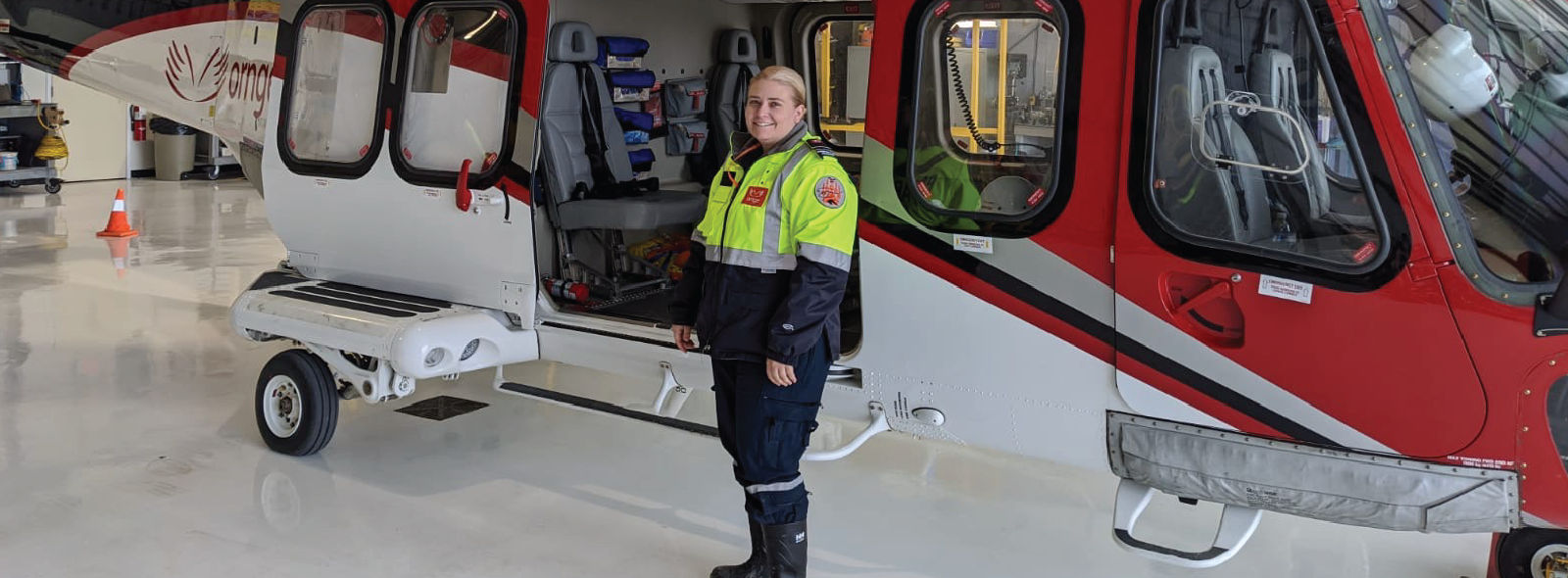 A paramedic in uniform standing in front of a red, blue, and white helicopter