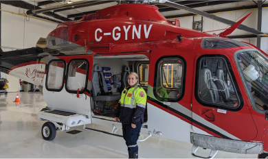 Un ambulancier en uniforme debout devant un hélicoptère rouge, bleu et blanc