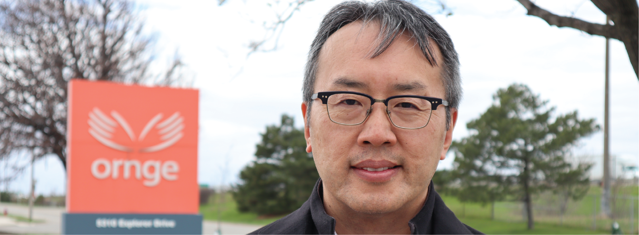 a man with glasses and a black coat standing in front of the Ornge building sign