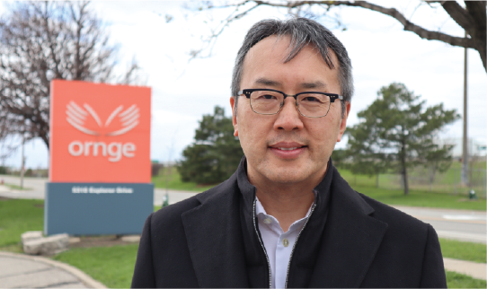 un homme avec des lunettes et un manteau noir debout devant le panneau du bâtiment Ornge