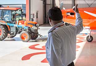 In foreground an Ornge staff person giving the thumbs up to a tractor driver in the background with a fixed wing Ornge plane nearby