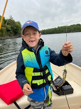 Child on a boat holding a small fish on a fishing line.