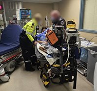 Paramedics providing care to a patient on a stretcher in a hospital room with medical equipment nearby.